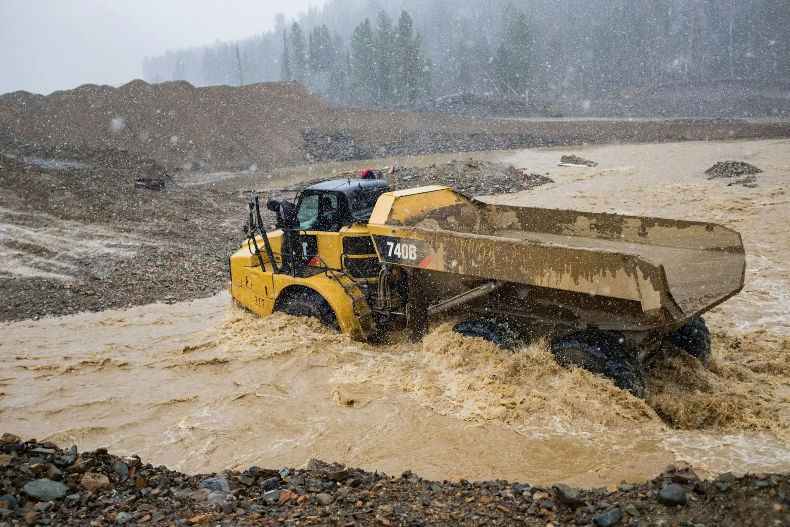 Articulated dump truck driving through deep muddy water in heavy rain